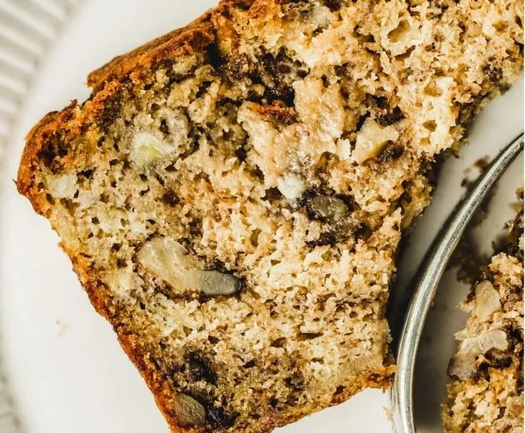 Loaf of freshly baked banana walnut bread with walnuts on a wooden table