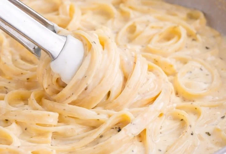 Homemade Alfredo sauce in a bowl with fresh herbs and pasta.