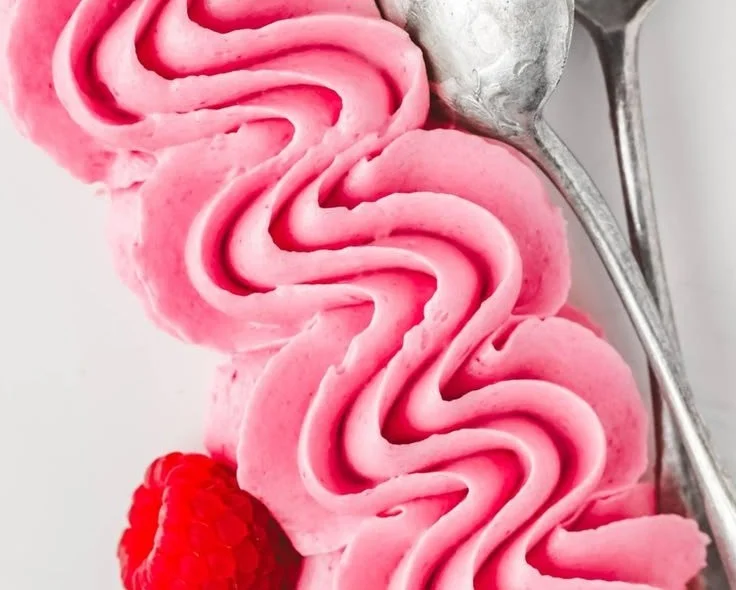 Bowl of homemade raspberry buttercream frosting with fresh raspberries on top