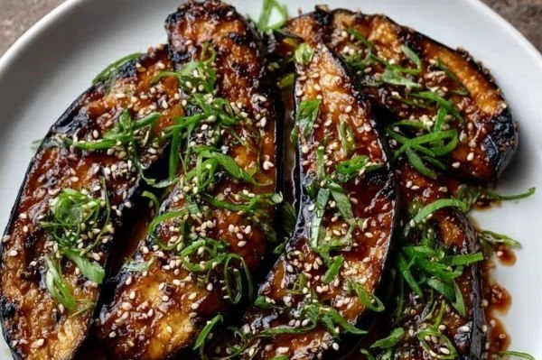 Miso-ginger glazed eggplant garnished with sesame seeds on a plate.