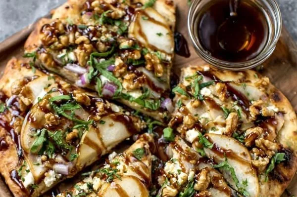 Pear, Walnut & Goat Cheese Flatbread drizzled with honey on a wooden platter.